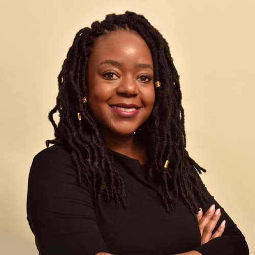 Portrait of a smiling woman with dreadlocks in black top.